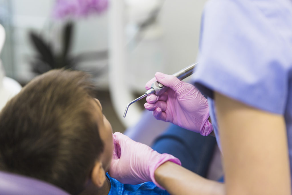 dentist checking boy's teeth with ultrasonic scaler